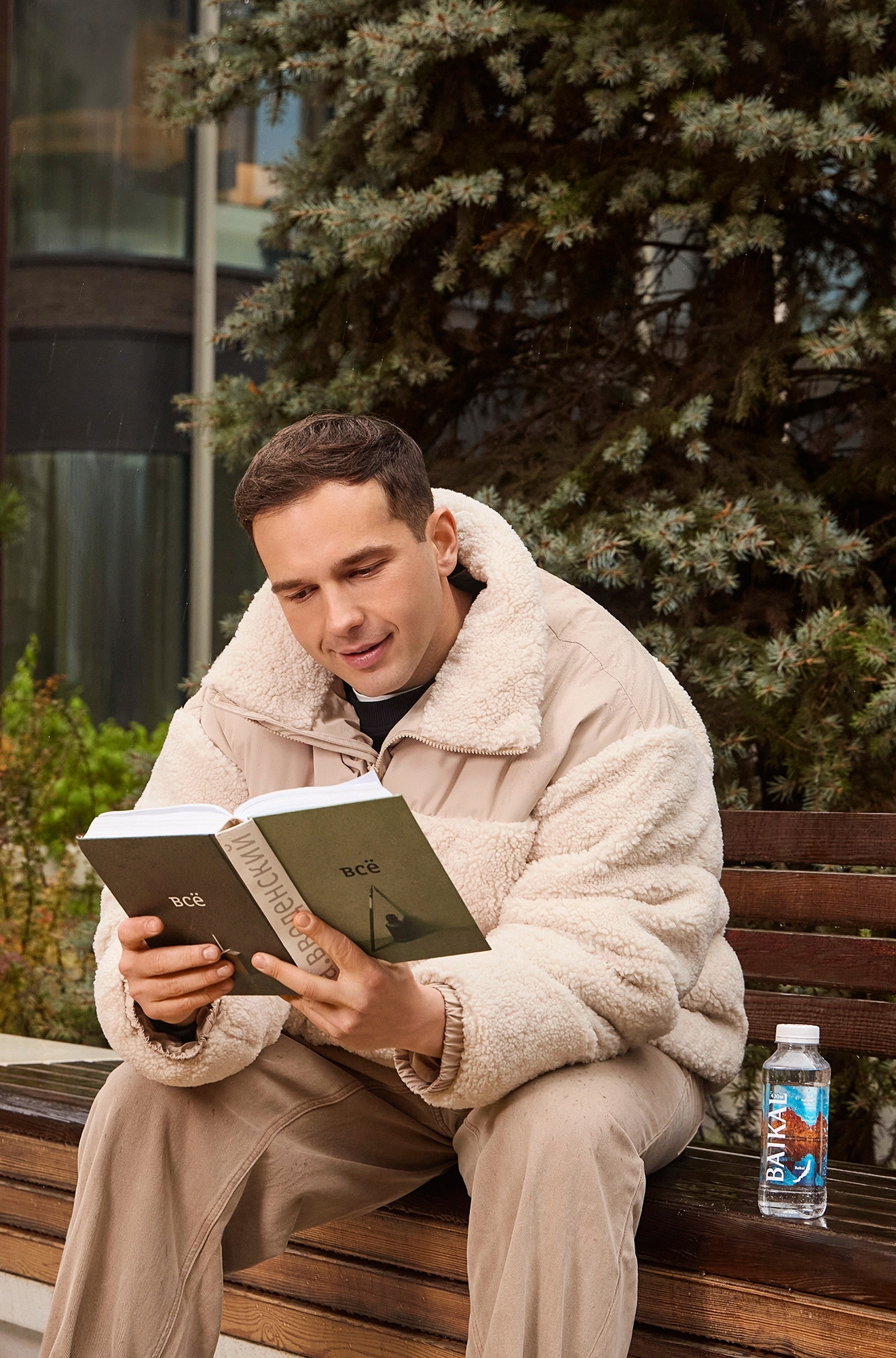 Фото парня, сидящего на земле рядом с велосипедом с бутылкой воды Байкал в руках